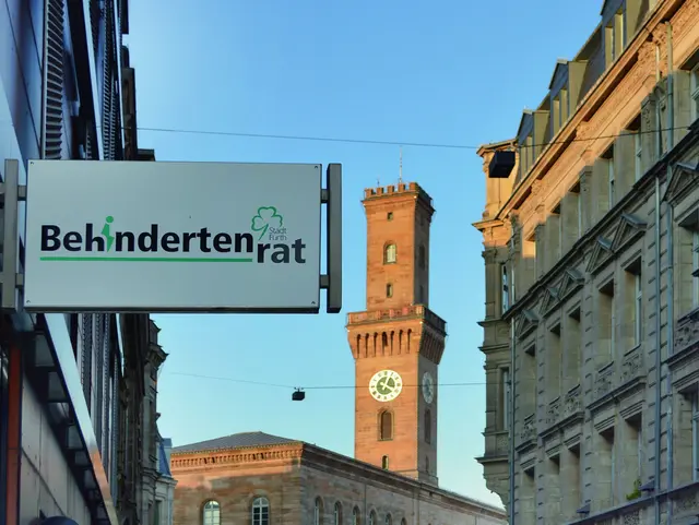 Schild mit der Aufschrift „Behindertenrat“, im Hintergund das Fürther Rathaus