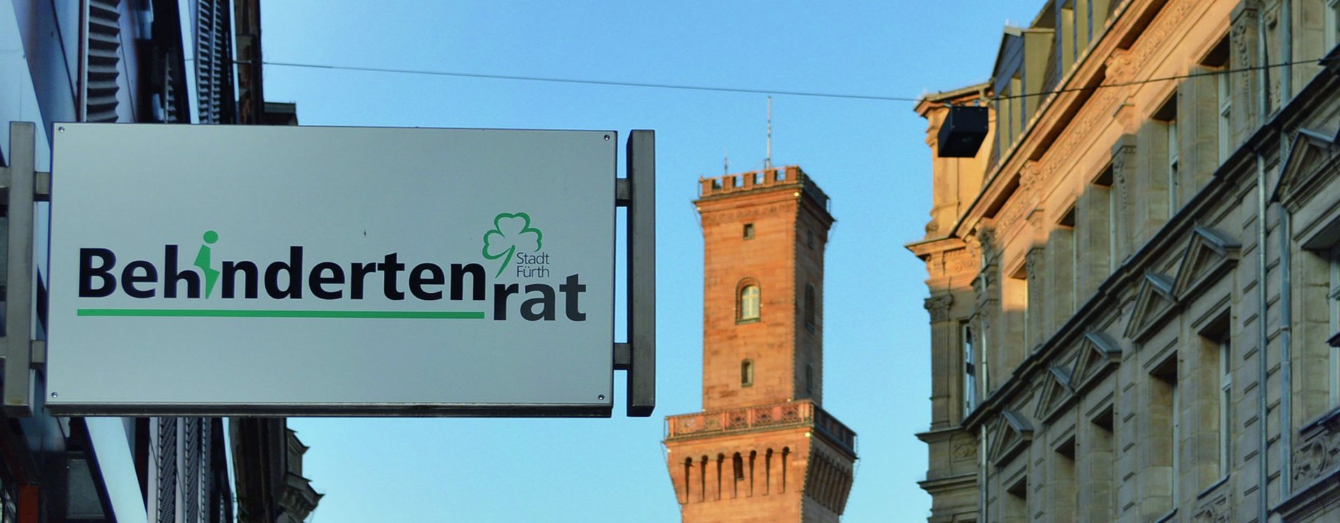 Schild mit der Aufschrift „Behindertenrat“, im Hintergund das Fürther Rathaus