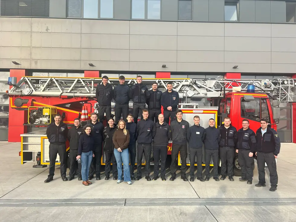 Mitarbeitende der Feuerwehr posieren vor einem Feuerwehrauto. Klick öffnet Bild in größerer Ansicht.