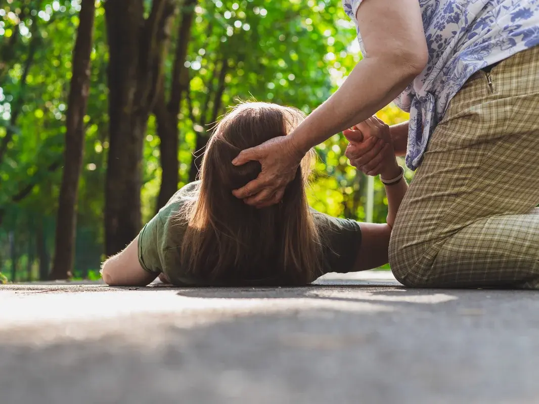 Eine ältere Frau hilft einer jüngeren Frau auf, die augenscheinlich durch Hitze erschöpft ist.