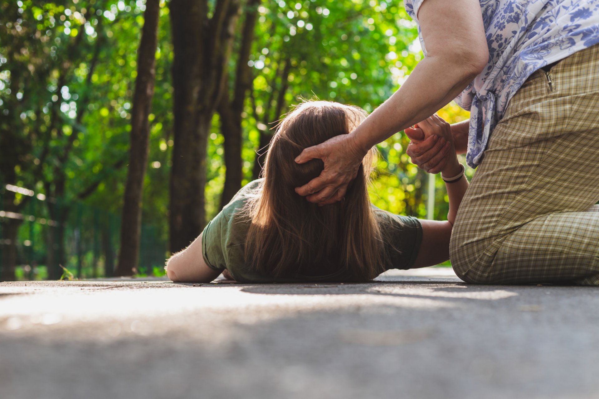 Eine ältere Frau hilft einer jüngeren Frau auf, die augenscheinlich durch Hitze erschöpft ist.