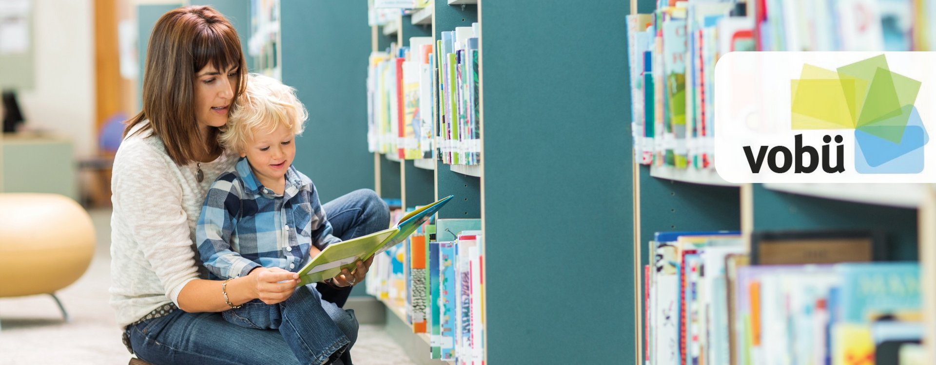 Junge Mutter liest ihrem Kind vor den Bücherregalen eine Bücherei vor. 