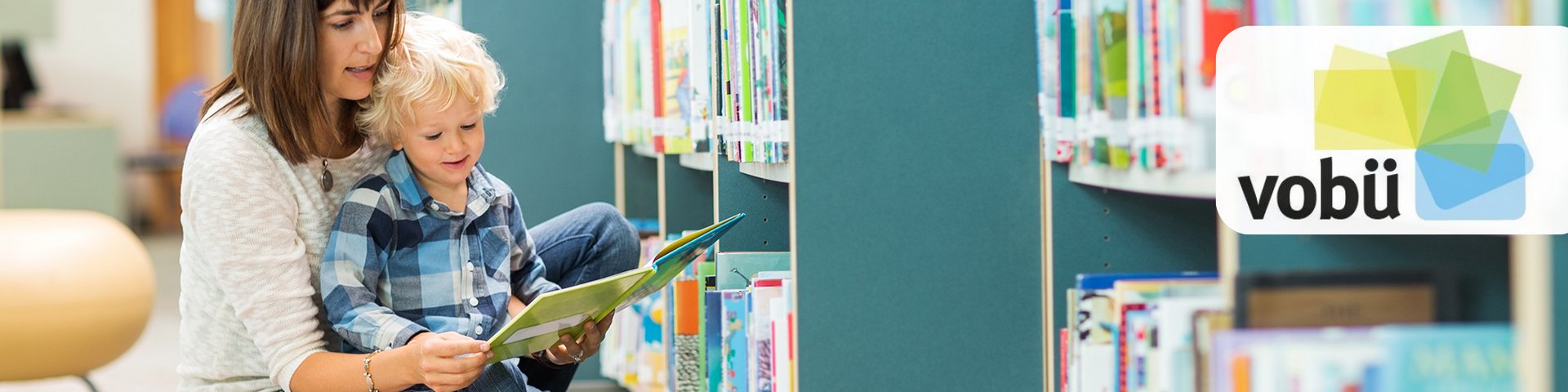 Junge Mutter liest ihrem Kind vor den Bücherregalen eine Bücherei vor. 