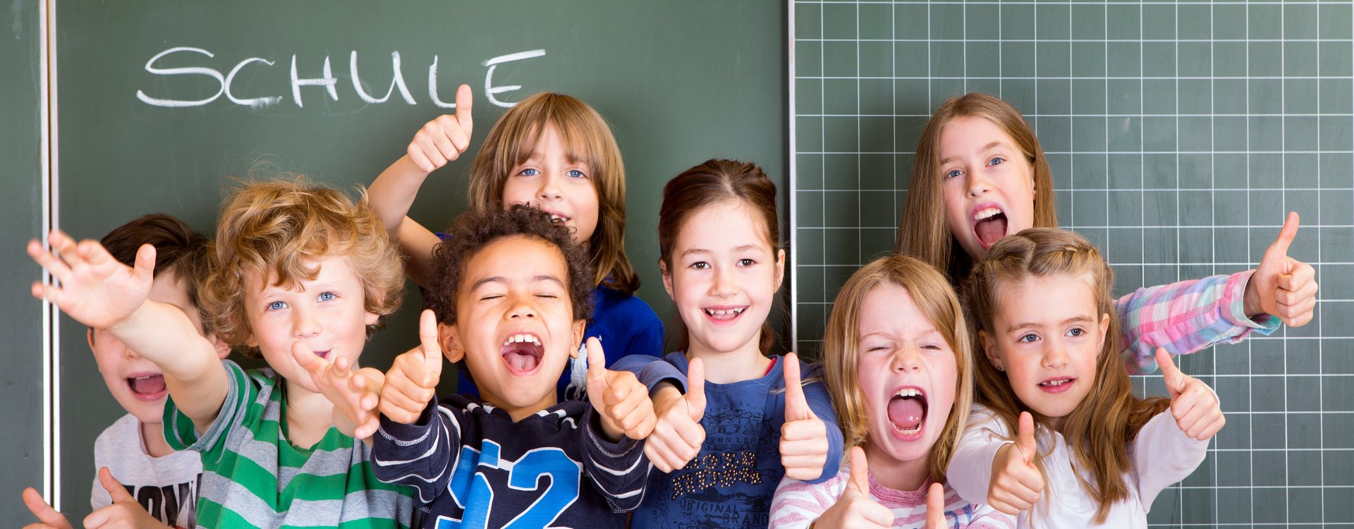 Eine Gruppe ausgelassener Schulkinder vor einer Schultafel.