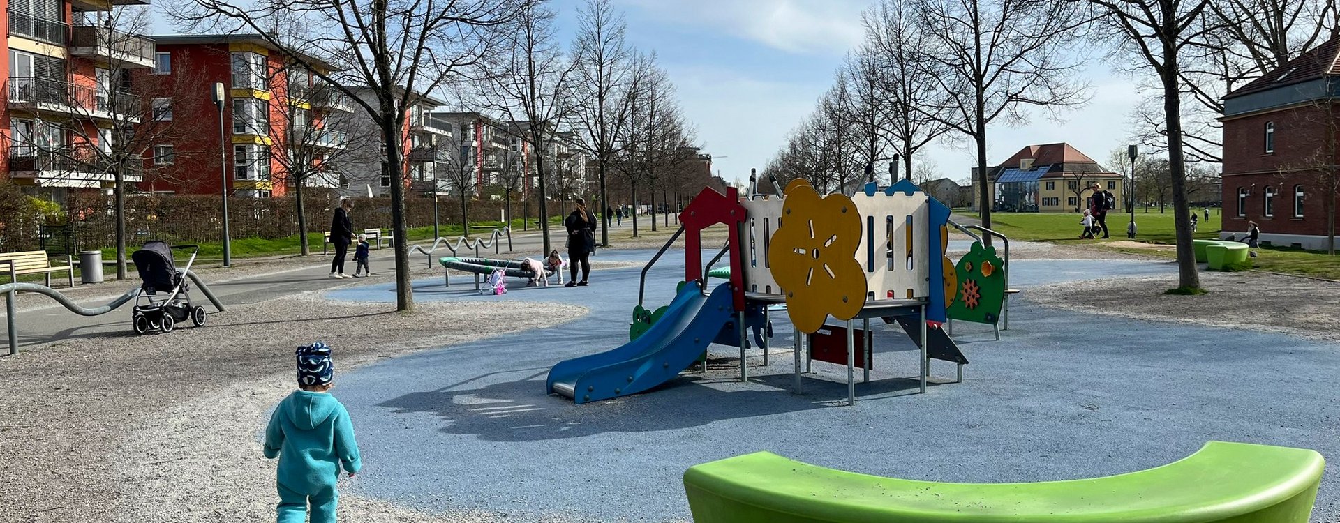 Ein Kleinkind in türkisem Anzug läuft auf den winterlichen Kleinkindspielplatz am Südstadtpark zu.