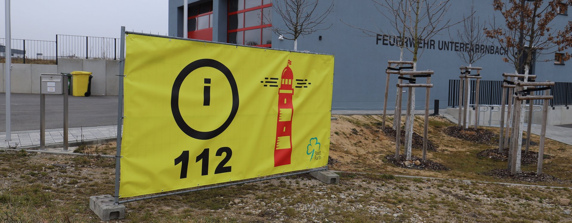 Gelbes Banner mit der Aufschrift "112" und einem Leuchtturm vor dem Feuerwehrgerätehaus Unterfarrnbach.