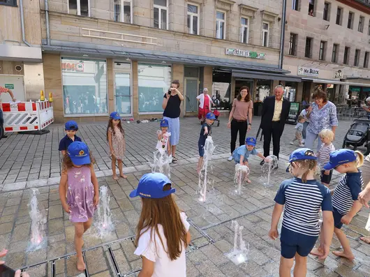 Kinder spielen mit den Fontänen des neuen Brunnens in der Fußgängerzone.