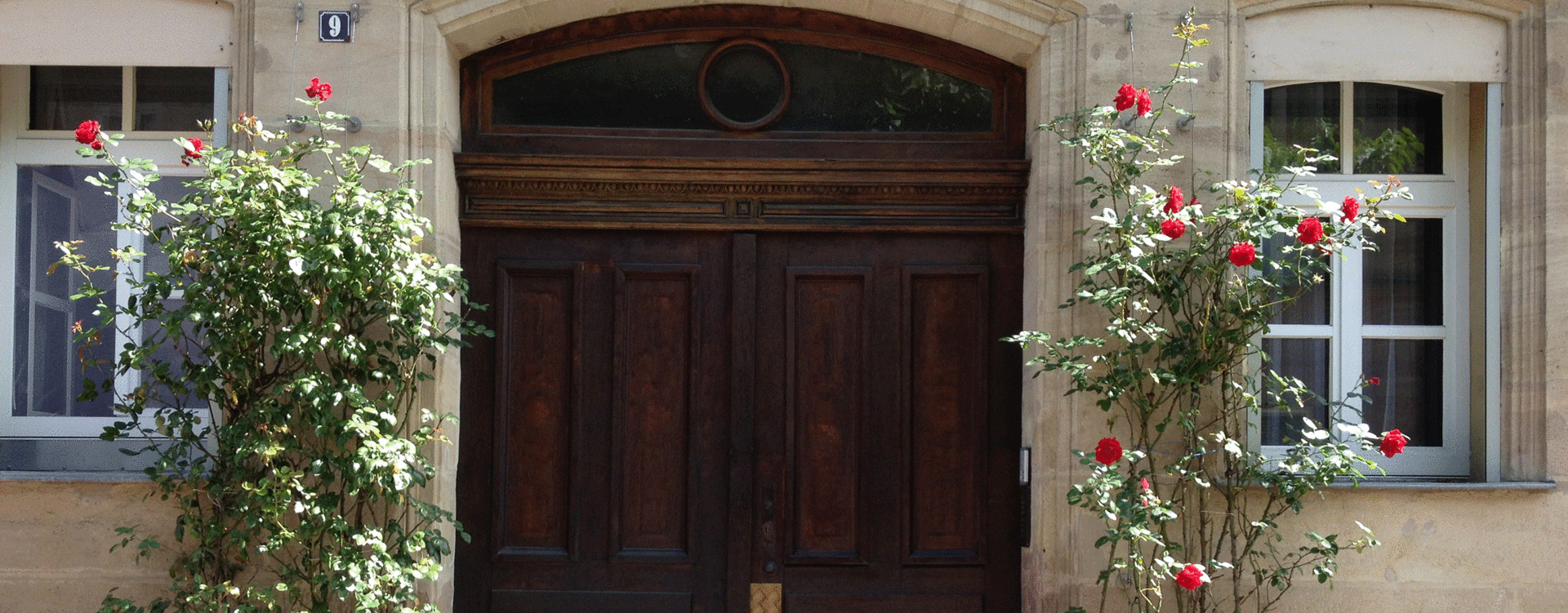 Ein rechts und links mit blühenden Kletterrosen begrünter Hauseingang.