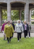 Seniorinnen und Senioren laufen auf die Kamera zu, im Rücken der Pavillon in der Konrad-Adenauer-Anlage