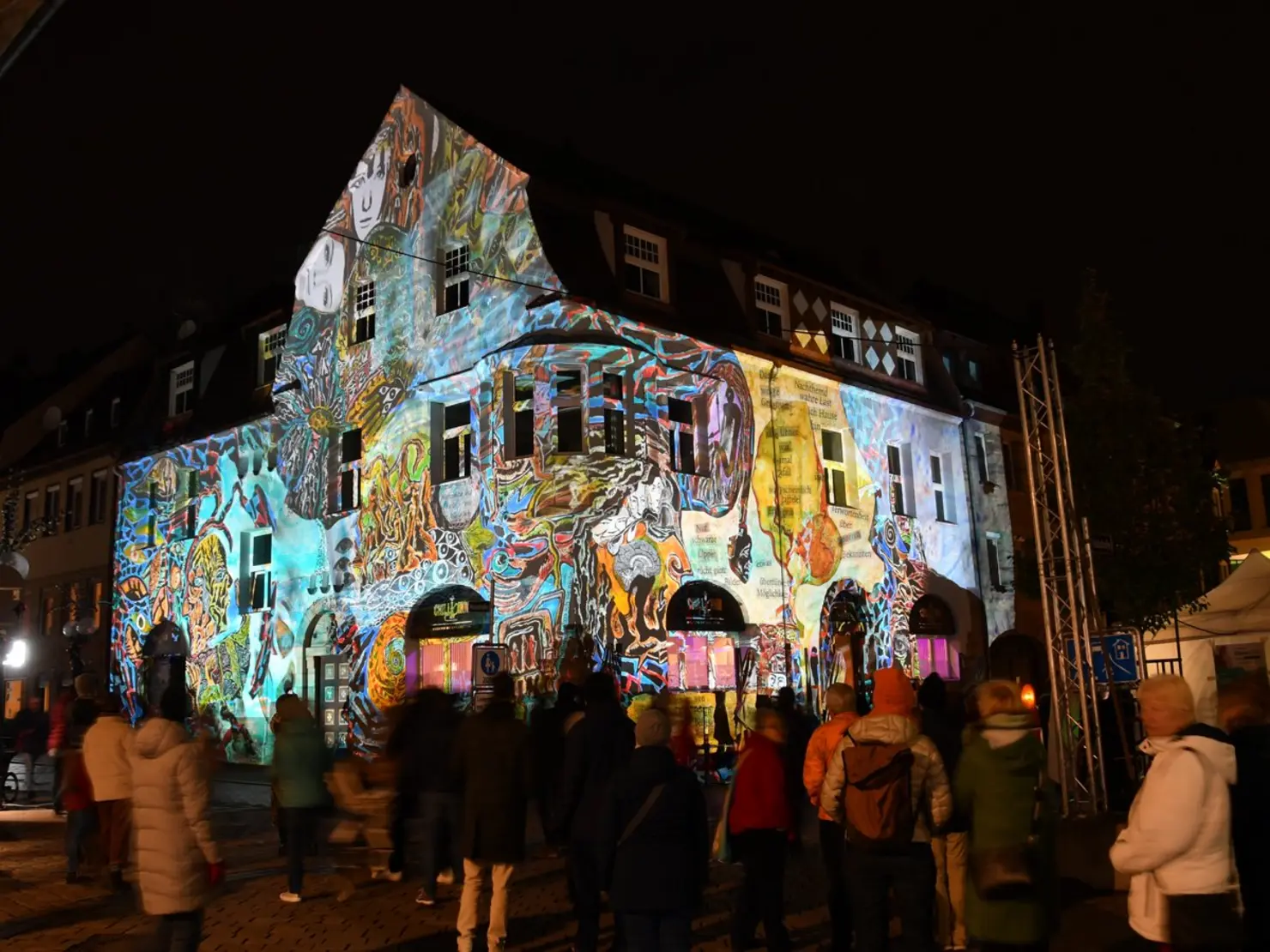 Besucherinnen und Besucher betrachten die illuminierte Fassade des Eckgebäudes in der Moststraße.