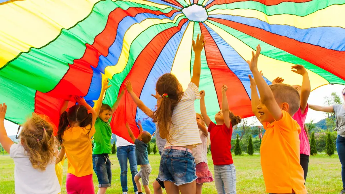 Lachende Kinder halten eine gestreifte Zeltplane in die Höhe