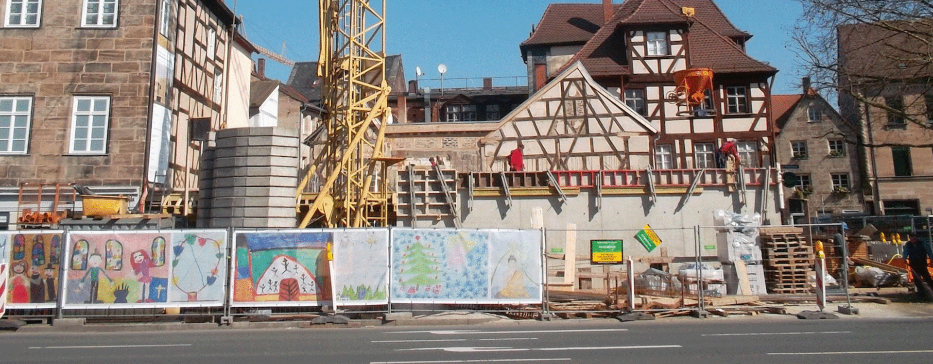 An einer Baustelle mit Kran wurde der Bauzaun von Kindern mit großformatigen Bildern gestaltet.