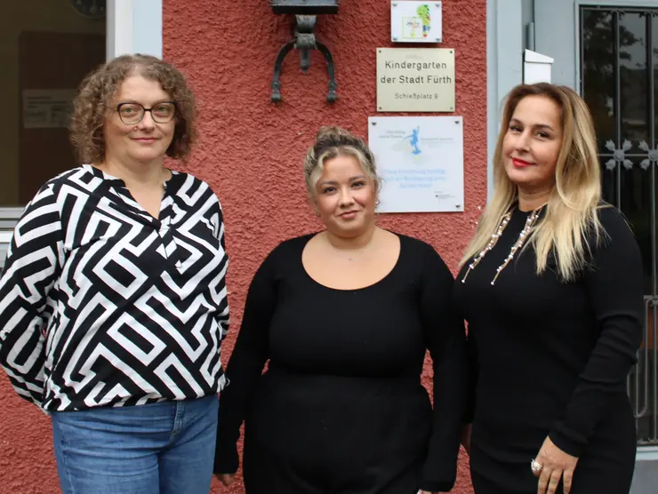 Drei Frauen vor einem rot gestrichenen Gebäude. Klick öffnet Bild in größerer Ansicht.