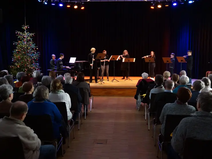 Musikschülerinnen und -schüler spielen auf einer mit einem Weihnachtsbaum geschmückten Bühne vor Publikum.