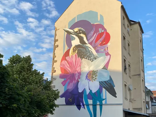 Großflächige Malerei an der Fassade eines vierstöckigen Hauses: Florale Motive und ein großer Eisvogel.