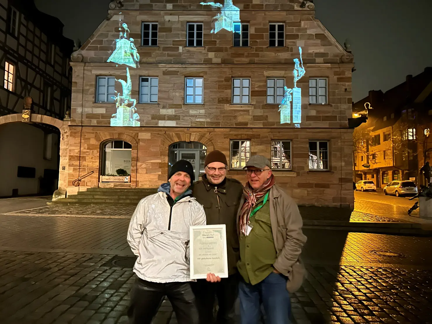 Das Künstlerkollektiv VEP Lichtbildklub freut sich vor dem illuminierten Gebäude am Marktplatz 2 über ihren Publikumspreis.