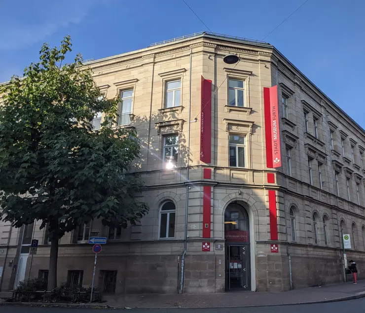 Außenansicht des Stadtmuseums: Ein zweistöckiges Eckgebäude mit historischer Fassade und rotem Banner mit der Aufschrift Stadtmuseum Fürth am Eingang.