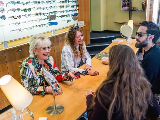 Beratungsgespräch bei einem Optiker: Ein junges Paar wird von zwei Fachhändlerinnen bei der Auswahl von Sonnenbrillen beraten. 