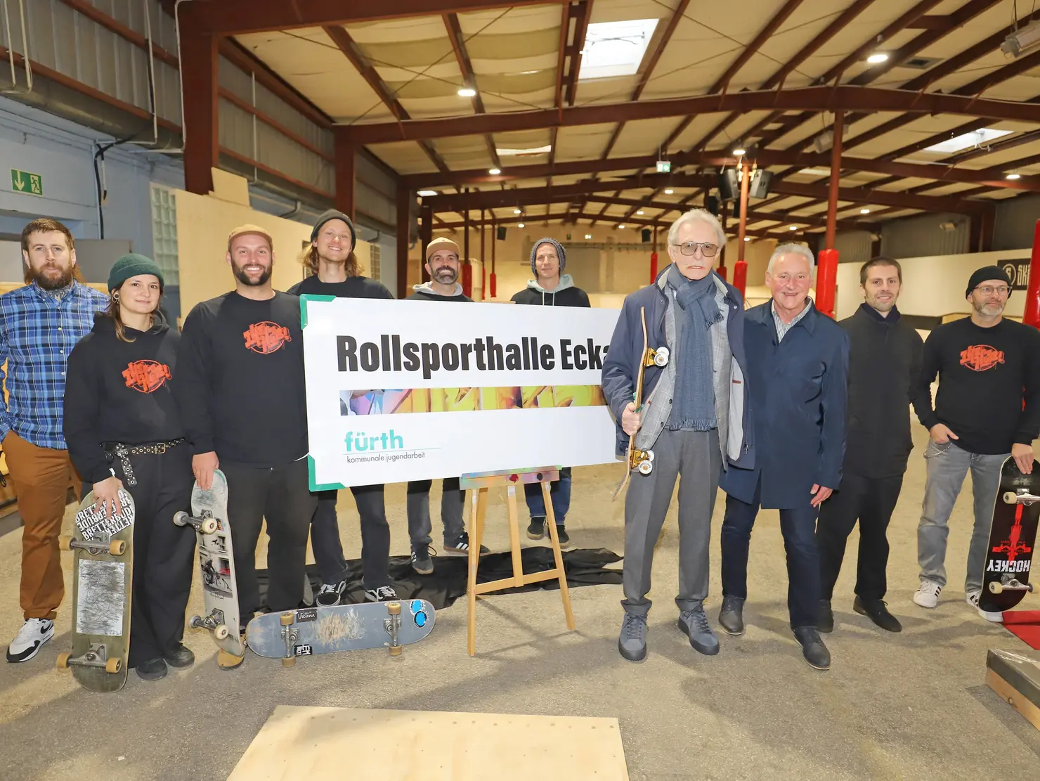 die beteiligten Personen stehen vor dem Schild mit der Aufschrift "Rollsporthalle Eckart"; Klick öffnet Bild in größerer Ansicht. 