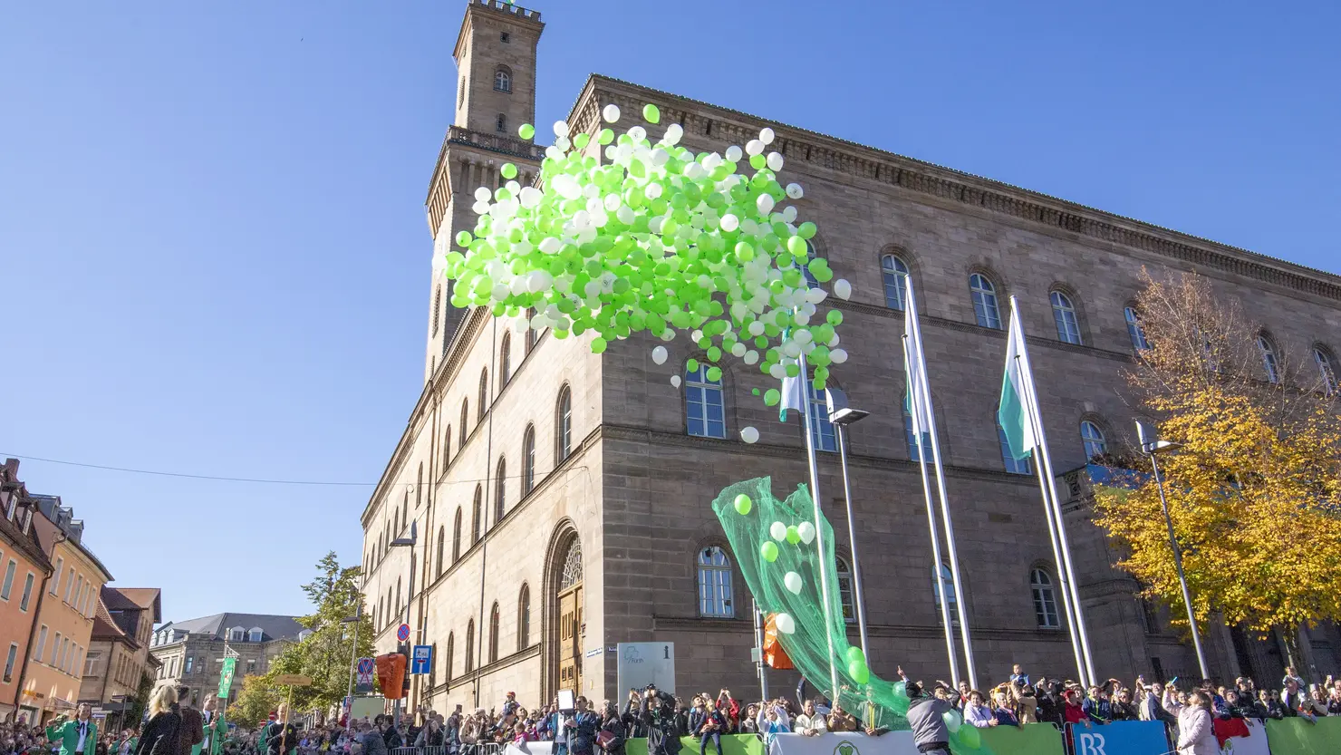 Grüne und weiße Luftballons steigen während des Erntedankfestzugs 2022 vor dem Rathaus in die Luft 