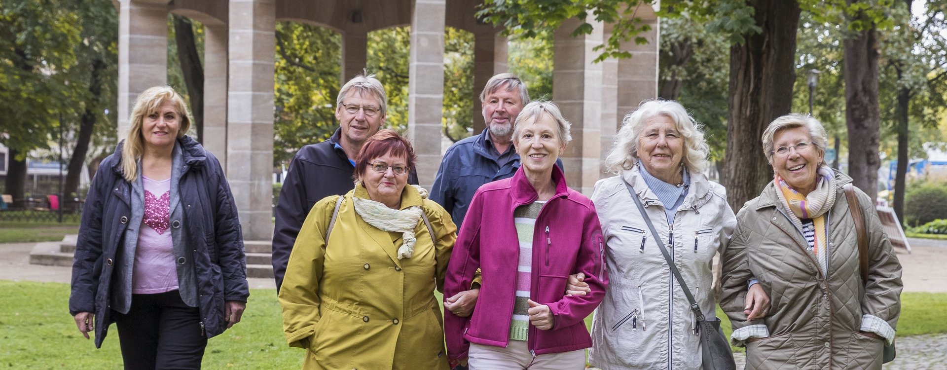 Seniorinnen und Senioren laufen auf die Kamera zu, im Rücken der Pavillon in der Konrad-Adenauer-Anlage