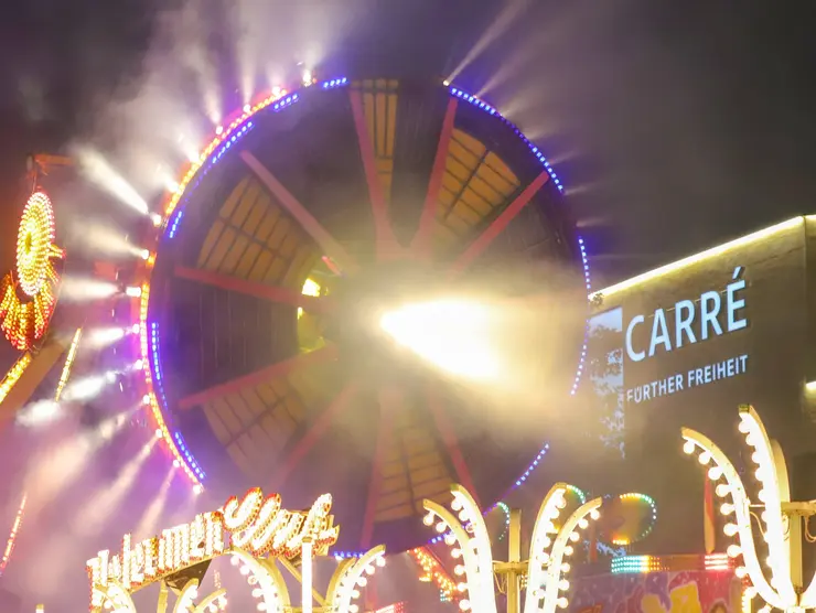 Fahrgeschäft mit vielen Lichtern bei Nacht vor dem Carré Fürther Freiheit