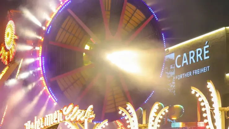 Fahrgeschäft mit vielen Lichtern bei Nacht vor dem Carré Fürther Freiheit