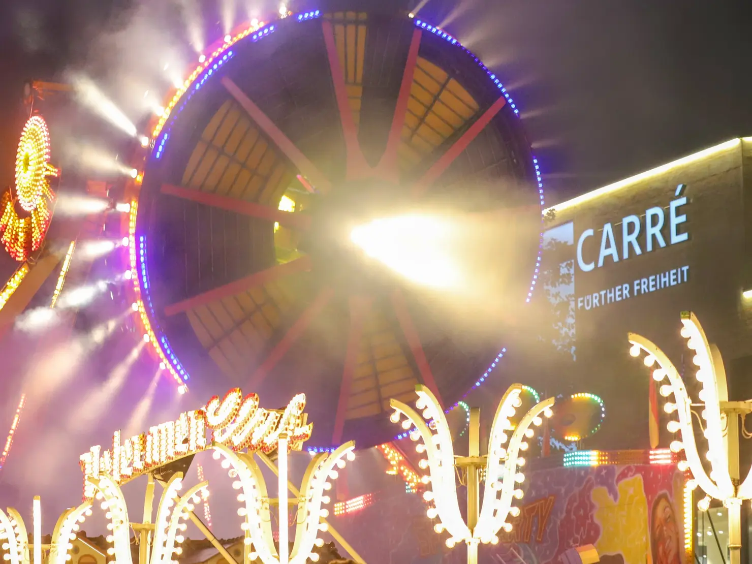 Fahrgeschäft mit vielen Lichtern bei Nacht vor dem Carré Fürther Freiheit