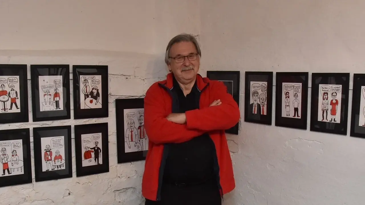 Der Künstler Gerhard Fuchs vor einer Wand mit Karikaturen.