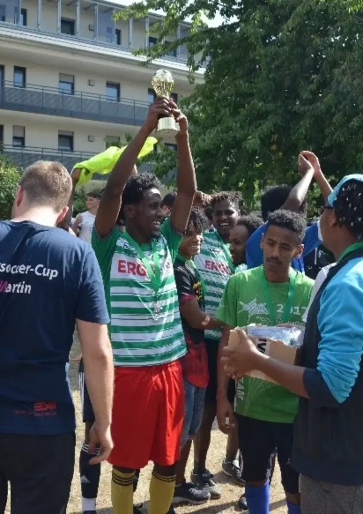 Ein strahlender Teilnehmer des Street Soccer Cups hält den Preis in die Luft, umgeben von seinen Team-Mitgliedern