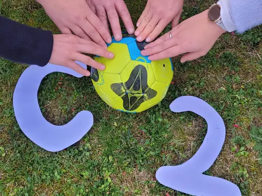 Fünf Hände ergreifen einen Ball der das O in CO2-Challenge darstellen soll. Klick öffnet Bild in größerer Ansicht.