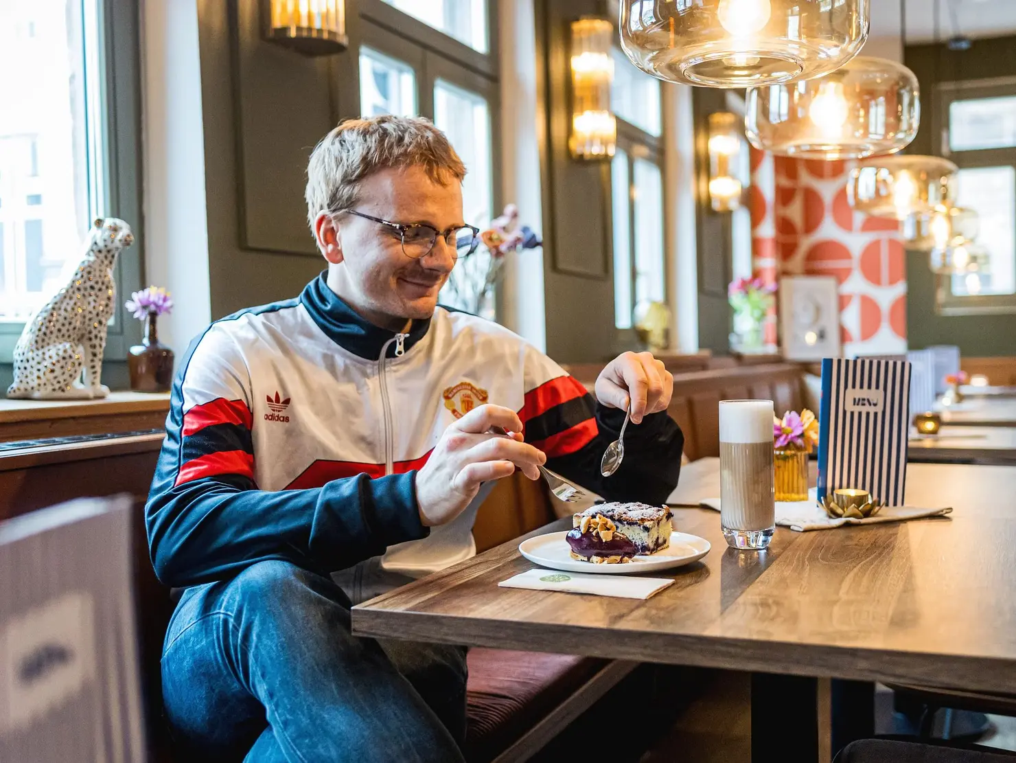 Ein junger Mann in einem hübschen Cafe genießt ein Stück Kuchen. Klick auf Bild öffnet Bildergalerie.