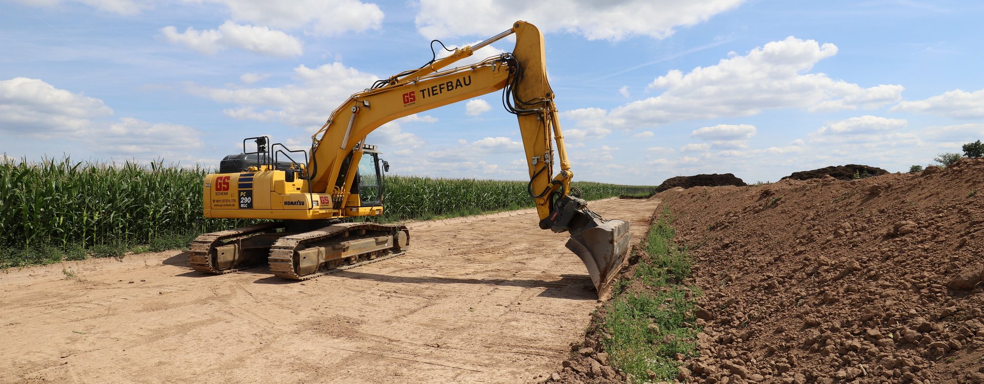 Bagger steht auf einem Baufeld, Mais im Hintergrund