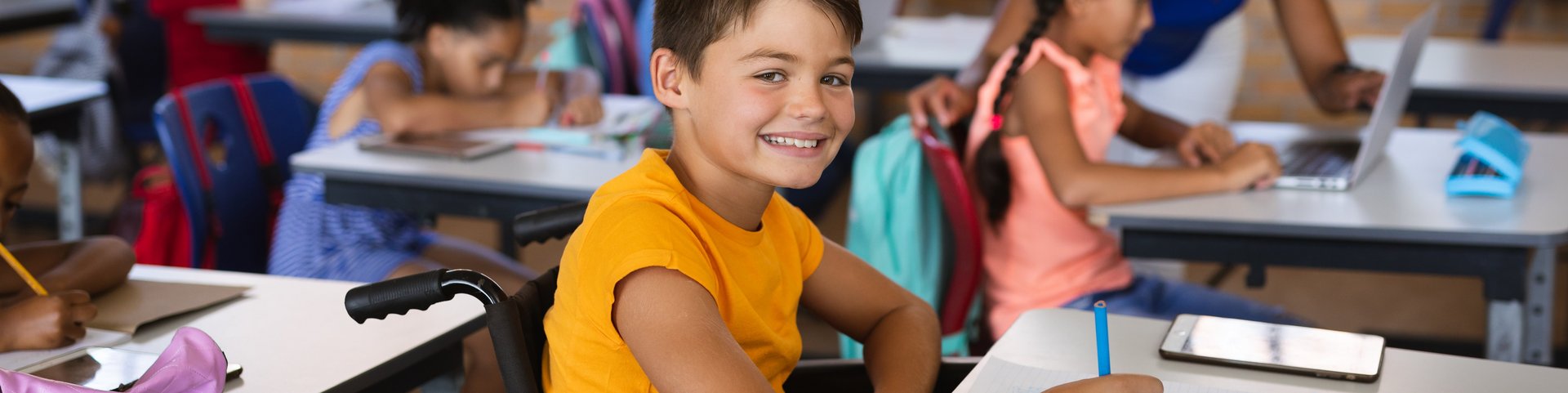 Portrait eines lachenden Jungen im Rollstuhl während einer Unterrichtsstunde in der Grundschule.