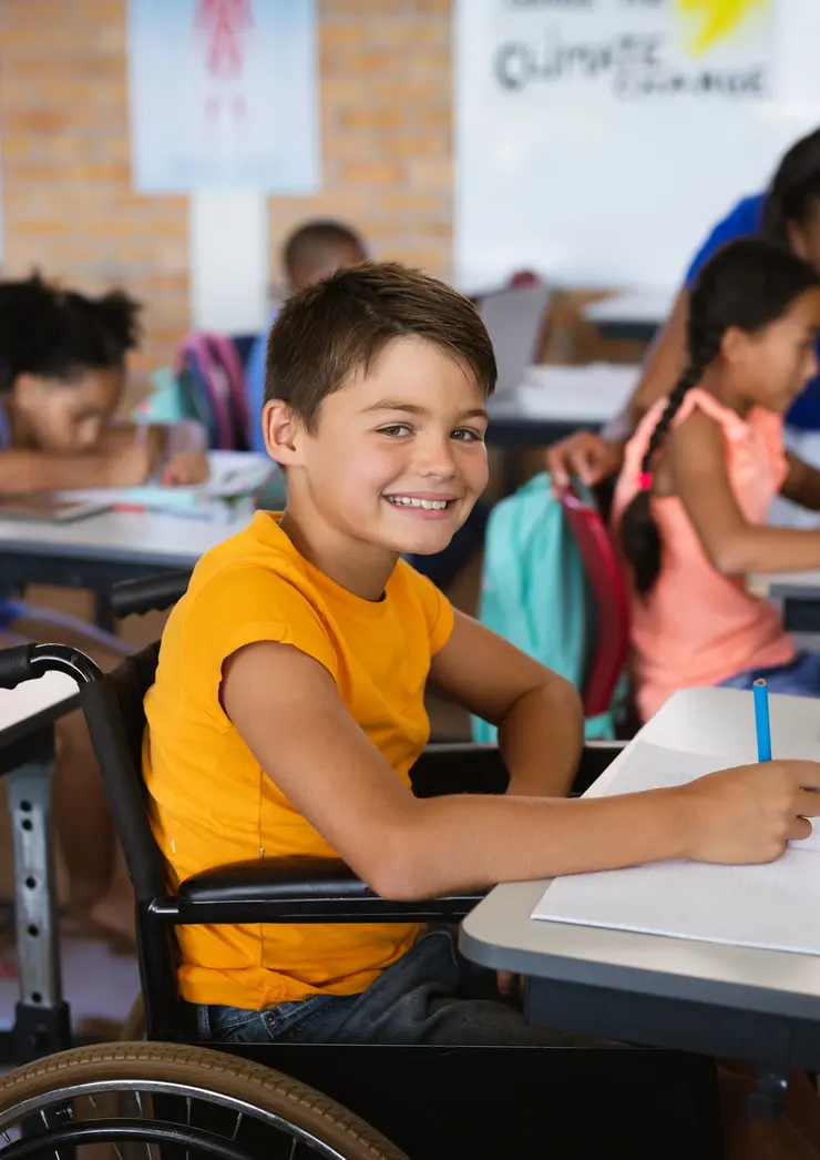 Portrait eines lachenden Jungen im Rollstuhl während einer Unterrichtsstunde in der Grundschule.