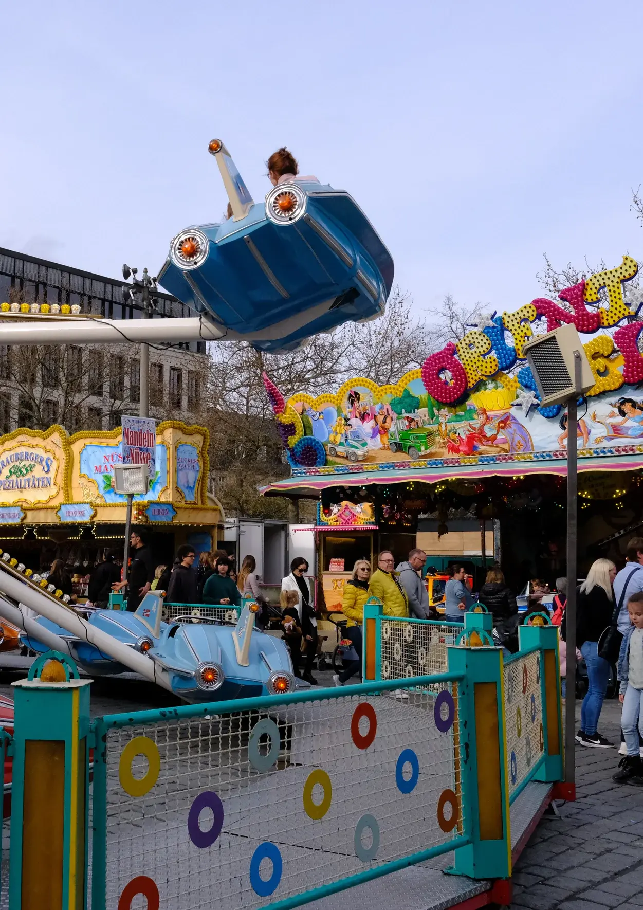 Fahrgeschäft und Menschen auf dem Frühlingsmarkt; Klick zeigt Bild in größerer Darstellung. 