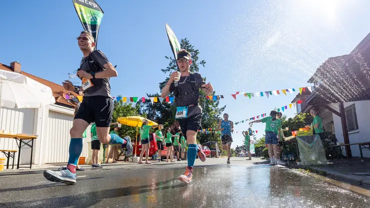 Zwei Läufer werden bei einer Getränkestation während des Metropolmarathons nassgespritzt.