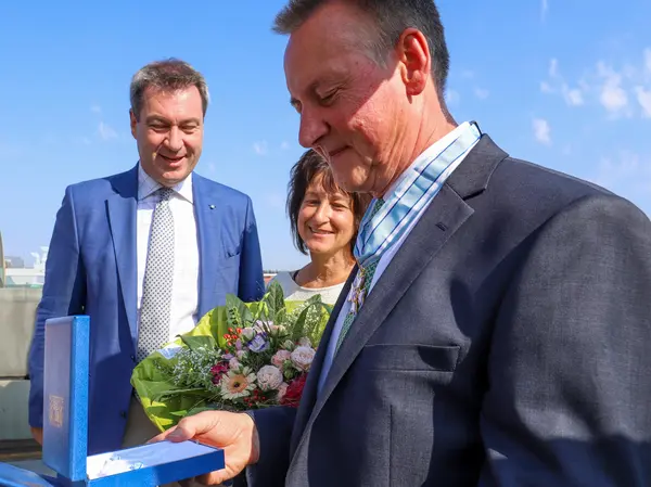 OB Jung betrachtet im Beisein von Ministerpräsident Söder und seiner Frau Heike den Bayerischen Verdienstorden. Klick öffnet Foto in Lightbox.