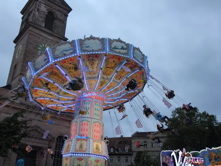 Das Kettenkarussell Volare vor der Kirche "Unsere Liebe Frau" bei Abend.