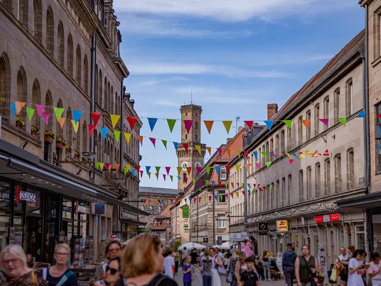 Die belebte Fußgängerzone mit dem Rathausturm im Hintergrund. Bunte Wimpel sind über die Straße gepannt.