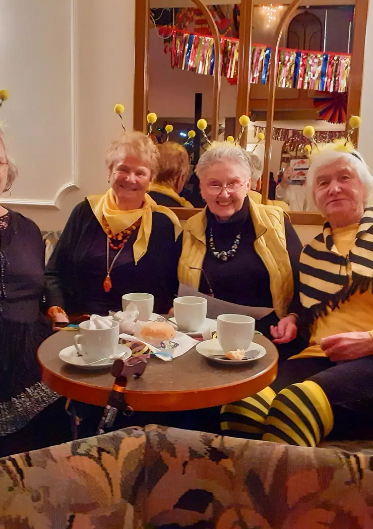 Als Bienen verkleidete Frauen sitzen auf einem Sofa um einen Kaffeetisch.