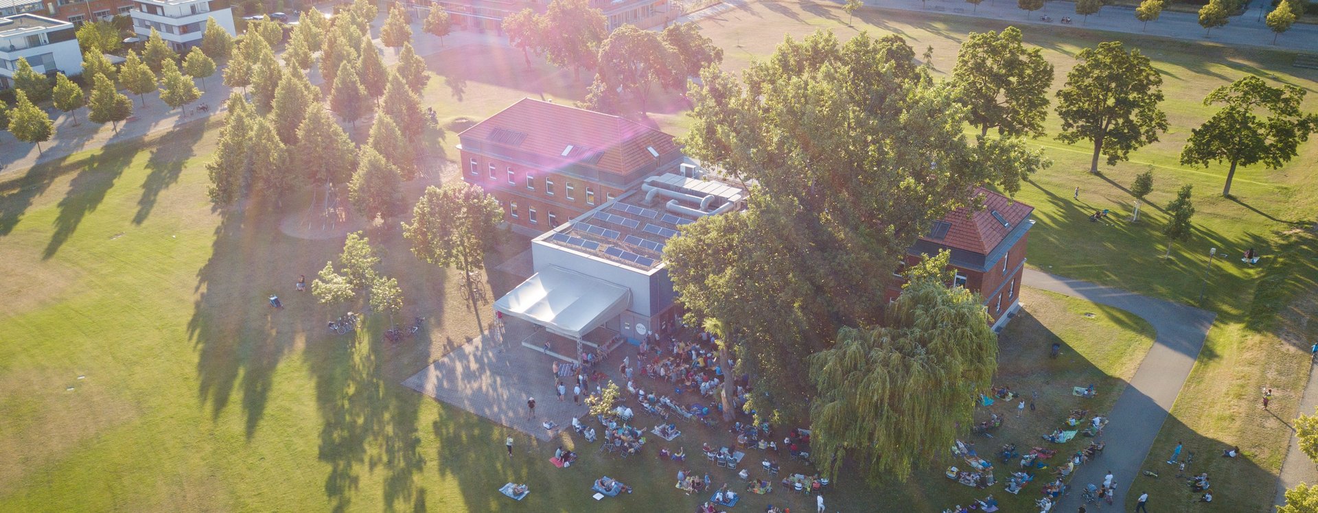 Luftaufnahme des gebäudes der Musikschule im Südstadtpark. Vor dem Haus findet ein Open-Air-Konzert mit Publikum statt.