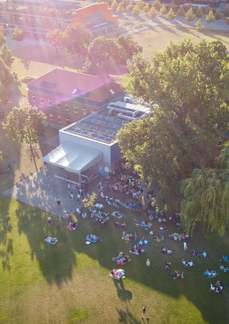 Luftaufnahme des gebäudes der Musikschule im Südstadtpark. Vor dem Haus findet ein Open-Air-Konzert mit Publikum statt.