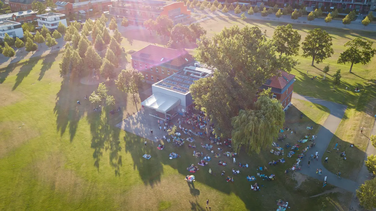 Luftaufnahme des gebäudes der Musikschule im Südstadtpark. Vor dem Haus findet ein Open-Air-Konzert mit Publikum statt.