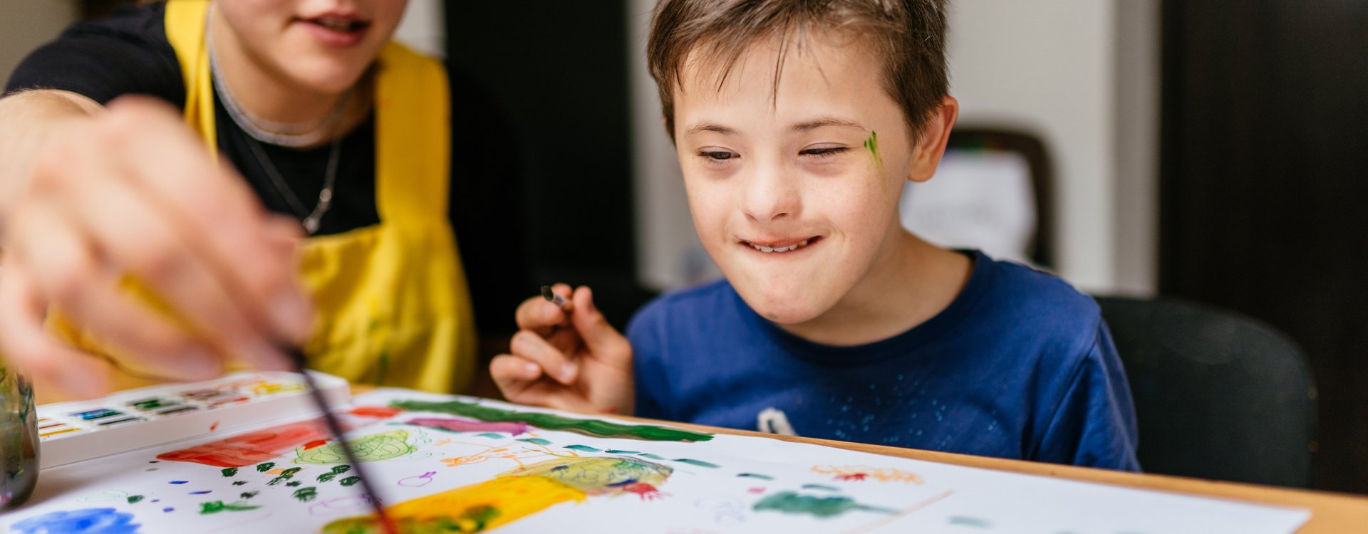 Eine Lehrerin malt zusammen mit einem Jungen mit Down-Syndrom