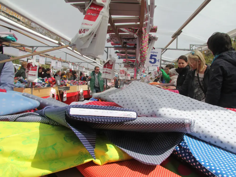 Bunte Stoffbahnen liegen auf einem Stand. Klick öffnet Bild in größerer Ansicht.