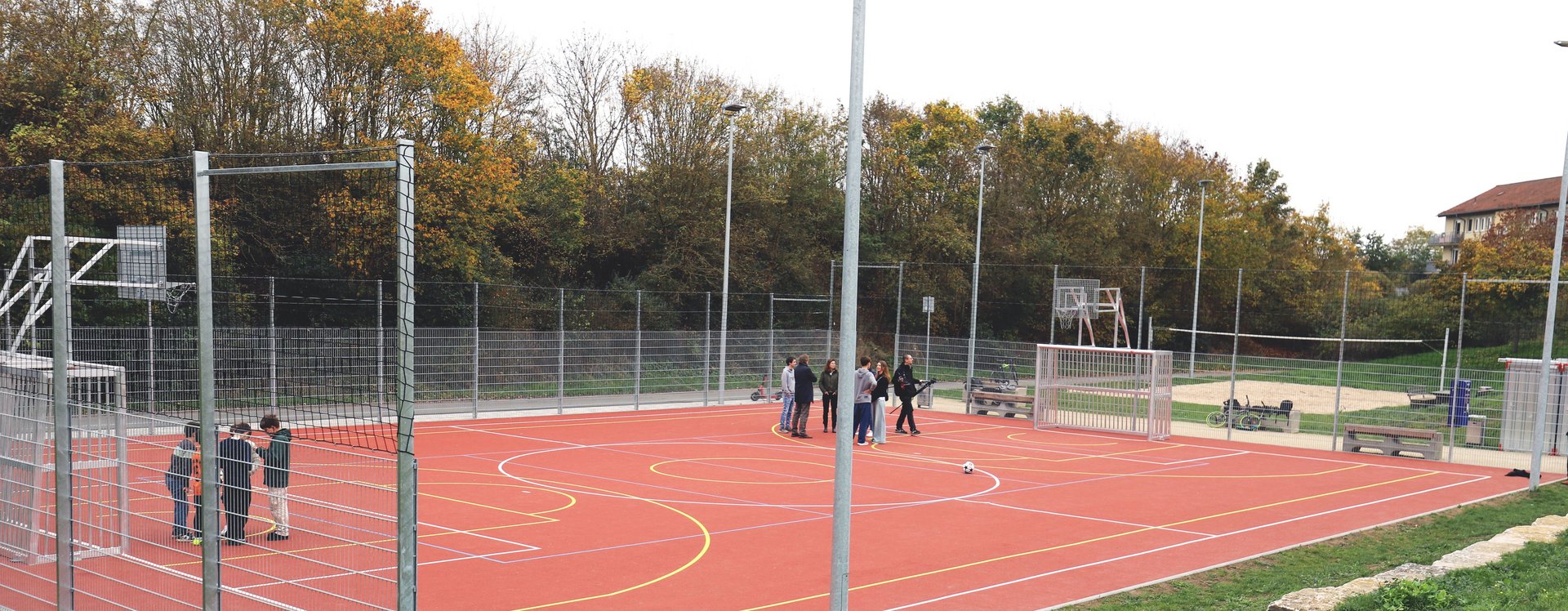 Sportfläche mit Basketballkörben und Toren auf roter Kunststofffläche.