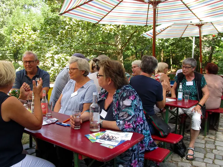 Seniorinnen und Senioren sitzen auf Bierbänken und unterhalten sich.