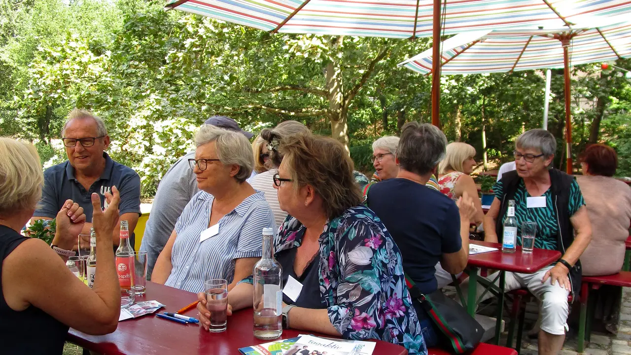 Seniorinnen und Senioren sitzen auf Bierbänken und unterhalten sich.