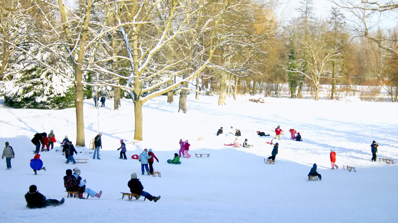 Kinder mit Schlitten am schneebedeckten Schlittenberg im Stadtpark. 